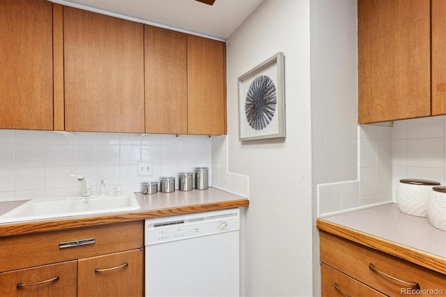 kitchen featuring brown cabinetry, decorative backsplash, white dishwasher, light countertops, and a sink