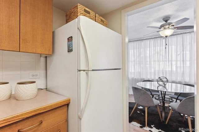 kitchen with tasteful backsplash, brown cabinetry, ceiling fan, freestanding refrigerator, and light countertops