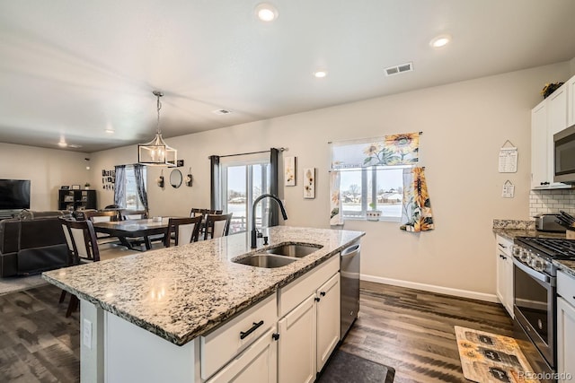 kitchen with sink, white cabinetry, stainless steel appliances, light stone countertops, and a center island with sink