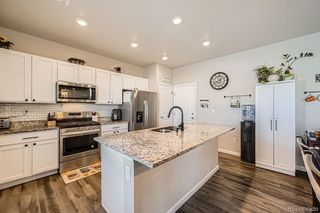 kitchen with appliances with stainless steel finishes, sink, white cabinets, light stone countertops, and a center island with sink