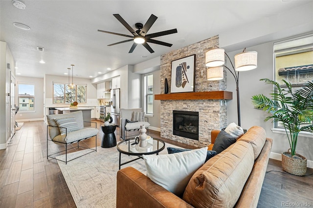 living room featuring baseboards, a ceiling fan, wood finished floors, and a fireplace