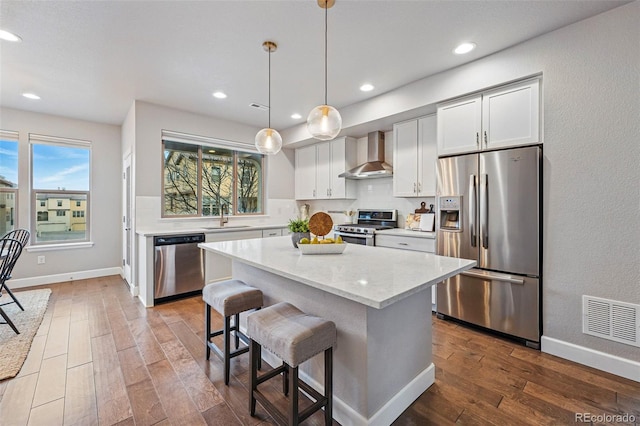 kitchen featuring visible vents, wall chimney exhaust hood, a sink, appliances with stainless steel finishes, and wood finished floors
