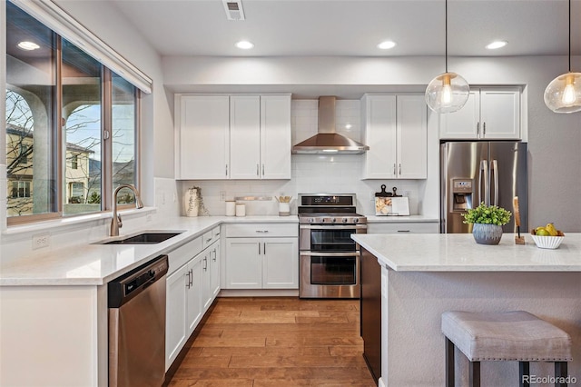 kitchen featuring visible vents, wall chimney exhaust hood, a sink, light wood-style floors, and stainless steel appliances