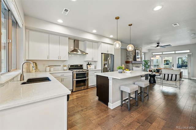 kitchen with tasteful backsplash, visible vents, wall chimney exhaust hood, a sink, and stainless steel appliances