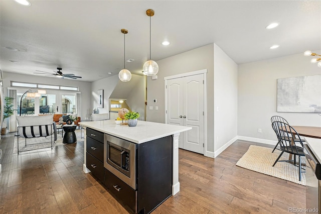 kitchen with stainless steel microwave, dark wood-type flooring, a center island, and light countertops