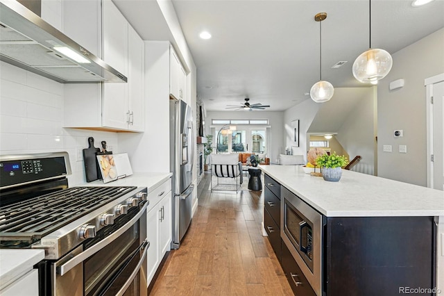 kitchen featuring wall chimney range hood, light countertops, light wood-style floors, white cabinetry, and stainless steel appliances