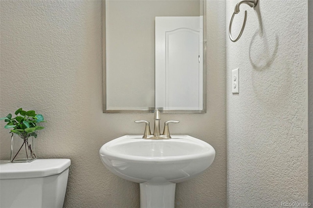 half bath featuring toilet, a textured wall, and a sink