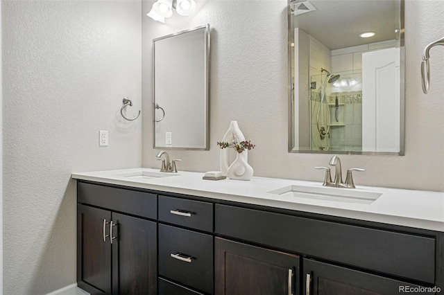 full bath featuring tiled shower, double vanity, a sink, and visible vents
