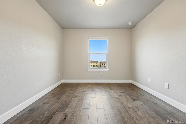 empty room featuring dark wood-type flooring and baseboards