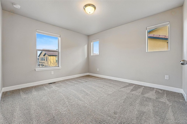 empty room featuring carpet flooring, visible vents, and baseboards