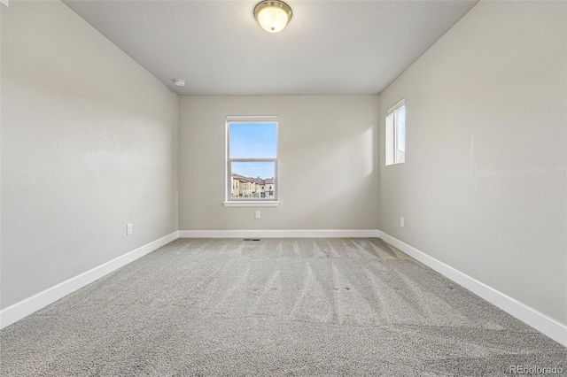 spare room with baseboards, plenty of natural light, and light colored carpet