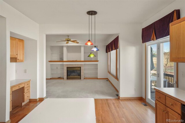 kitchen with decorative light fixtures, a tile fireplace, light hardwood / wood-style floors, and ceiling fan