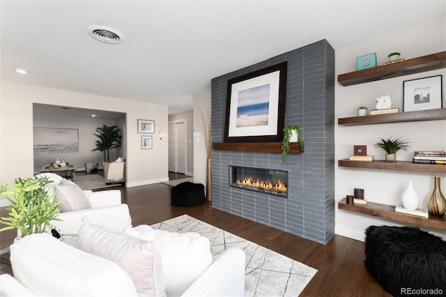 living room with a tile fireplace and dark wood-type flooring