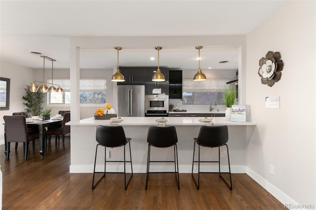 kitchen with hanging light fixtures, kitchen peninsula, a kitchen bar, high quality fridge, and dark hardwood / wood-style floors