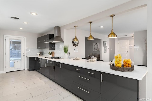 kitchen with stainless steel gas cooktop, kitchen peninsula, decorative backsplash, wall chimney range hood, and decorative light fixtures