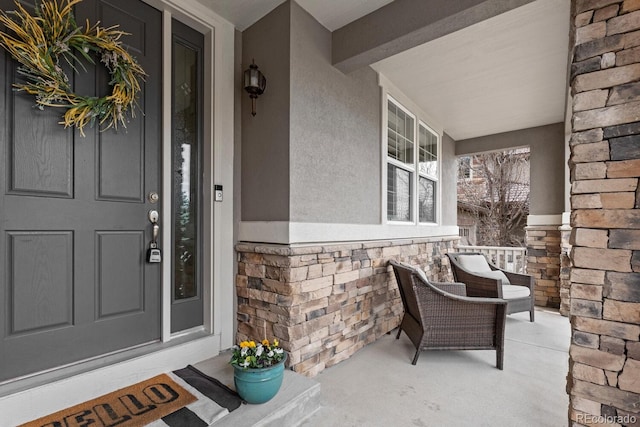 doorway to property featuring stone siding, a porch, and stucco siding