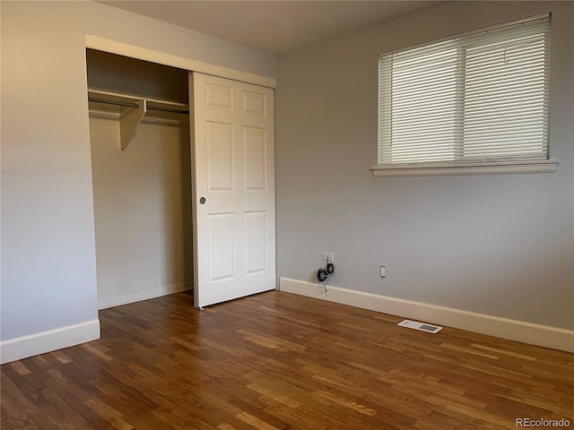 unfurnished bedroom with a closet, wood finished floors, visible vents, and baseboards