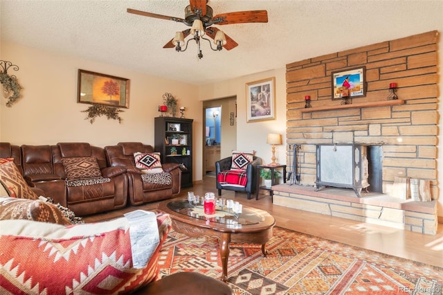 living room with ceiling fan, wood finished floors, a textured ceiling, and a stone fireplace