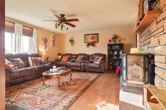 living area featuring a textured ceiling, a fireplace, a ceiling fan, and wood finished floors