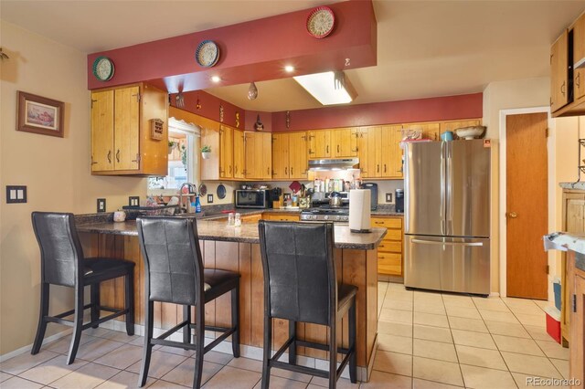 kitchen featuring dark countertops, stainless steel appliances, light tile patterned floors, and a peninsula