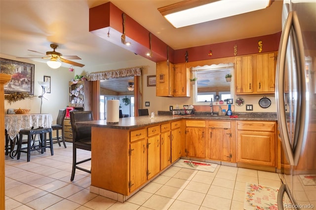 kitchen featuring light tile patterned floors, a peninsula, a sink, and freestanding refrigerator