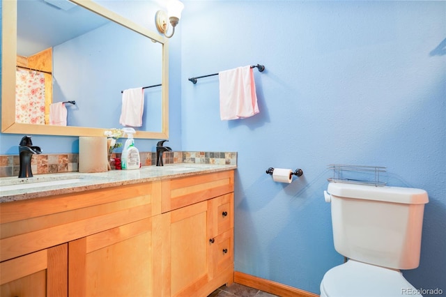 bathroom with baseboards, a sink, toilet, and double vanity