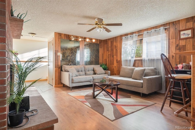 living room featuring a textured ceiling, ceiling fan, wooden walls, and wood finished floors