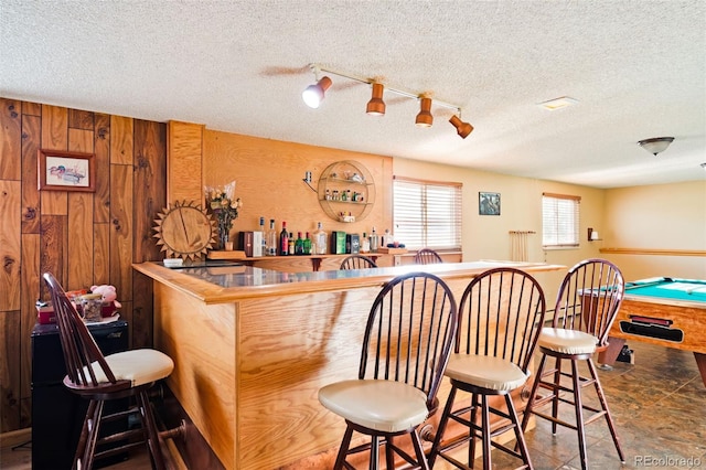 bar featuring a bar, wooden walls, and a textured ceiling