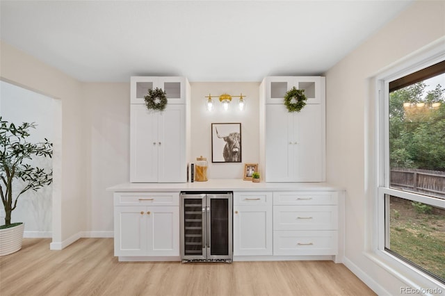 bar with wine cooler, white cabinets, and light wood-type flooring