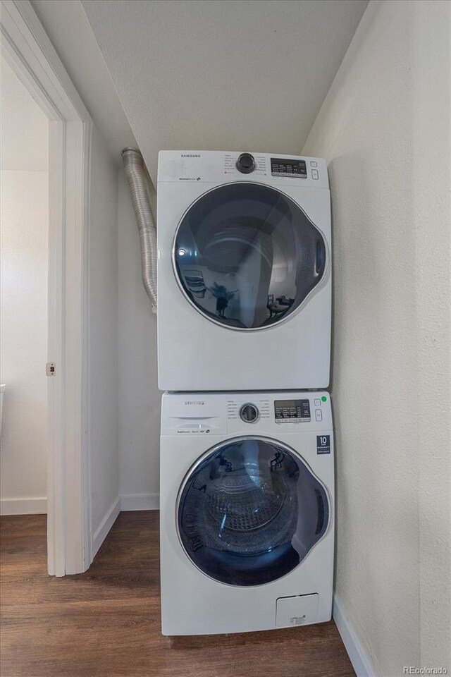 laundry room with stacked washer and clothes dryer, baseboards, and wood finished floors