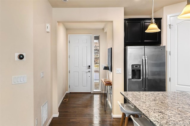 kitchen featuring a breakfast bar area, hanging light fixtures, light stone countertops, stainless steel fridge, and dark hardwood / wood-style floors