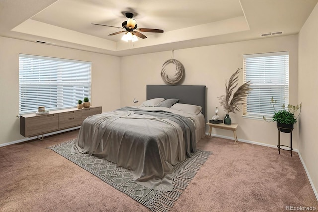 carpeted bedroom with ceiling fan and a tray ceiling