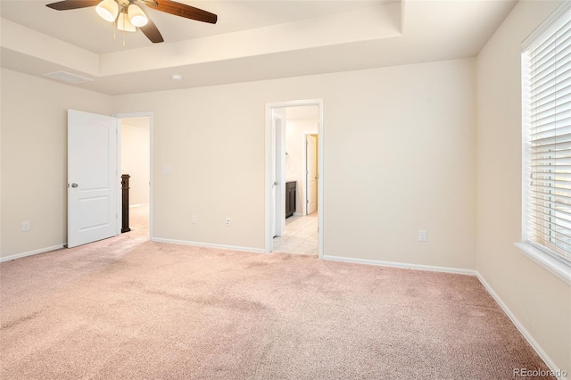 spare room featuring ceiling fan, light carpet, and a raised ceiling