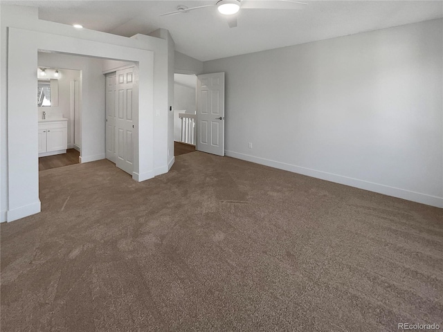 unfurnished bedroom featuring dark carpet, vaulted ceiling, ceiling fan, and ensuite bath