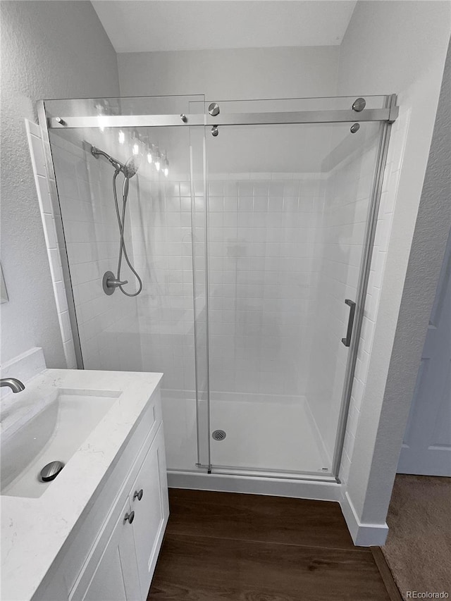 bathroom with wood-type flooring, a shower with door, and vanity