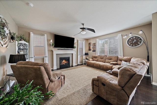 living room featuring a tile fireplace, baseboards, ceiling fan, and dark wood-style flooring