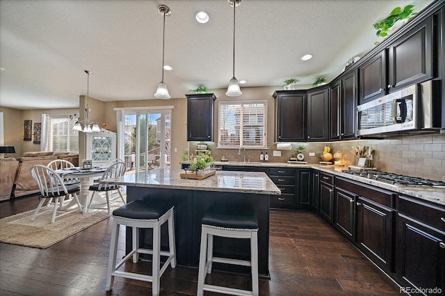 kitchen with light stone counters, dark wood-style floors, open floor plan, stainless steel appliances, and decorative backsplash