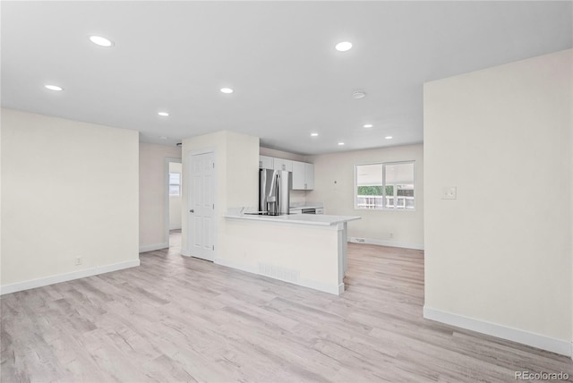 kitchen featuring white cabinets, stainless steel refrigerator with ice dispenser, light hardwood / wood-style floors, and kitchen peninsula