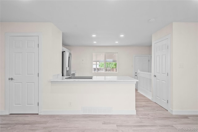 kitchen featuring stainless steel fridge, kitchen peninsula, and light wood-type flooring