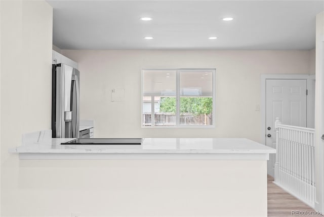 kitchen featuring light hardwood / wood-style flooring, kitchen peninsula, stainless steel fridge, white cabinets, and light stone counters