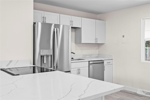 kitchen with appliances with stainless steel finishes, white cabinetry, sink, light hardwood / wood-style floors, and light stone counters