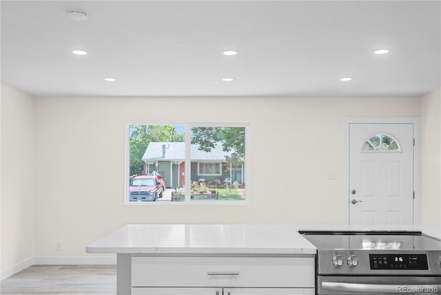 kitchen with light stone counters, light hardwood / wood-style flooring, stainless steel range, and white cabinets