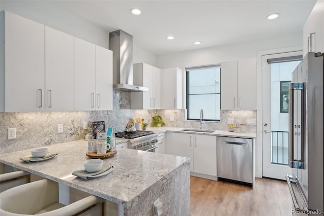 kitchen with light hardwood / wood-style floors, high end appliances, wall chimney exhaust hood, white cabinets, and sink