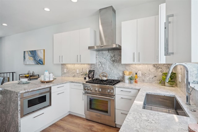 kitchen featuring light hardwood / wood-style flooring, tasteful backsplash, wall chimney exhaust hood, high end stainless steel range, and sink