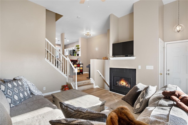 living room with a tile fireplace, wood-type flooring, and ceiling fan