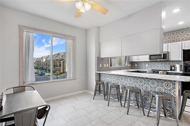 kitchen with appliances with stainless steel finishes, white cabinets, backsplash, kitchen peninsula, and a breakfast bar area