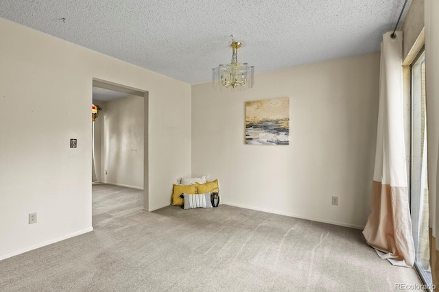 spare room with carpet floors, a textured ceiling, and a notable chandelier