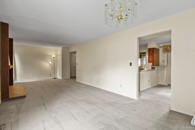 spare room featuring light colored carpet, a textured ceiling, and an inviting chandelier