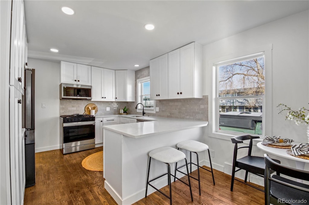 kitchen featuring white cabinets, dark hardwood / wood-style flooring, stainless steel appliances, tasteful backsplash, and kitchen peninsula