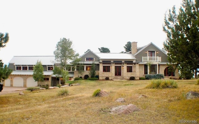 view of front of home featuring a balcony, driveway, a chimney, and a front lawn